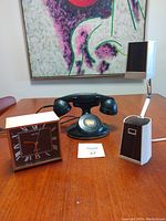 Photo showing the three items on a table: white lamp with dark wood accents, black rotary phone, and Seiko clock