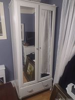 Full view of the white wooden wardrobe with two mirrored front doors and a single drawer at the bottom.