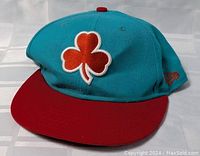 Front view of Boston Celtics hat showing red shamrock embroidered on teal crown and red brim.