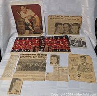 Entire lot of vintage Detroit Red Wings newspaper cutouts and photos laid out on white fabric background, featuring multiple items including Gordie Howe photo and team pictures.