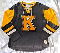 Front angled view of Kingston Frontenacs hockey sweater in black with large yellow K and yellow sleeves with stripe detailing.