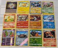 Top-down photo of 12 Pokémon cards laid out in a 3x4 grid showing holo and regular cards including Pikachu, Charmander, and Reshiram.