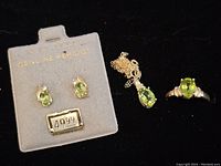 Photo of earrings on grey card marked 'Genuine Peridot' and price tag 49.99, lying next to necklace and ring on black background.