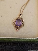 Front of oval amethyst pendant on gold chain displayed in jewelry box