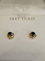 Photo of pair of gold earrings with blue stone on white fabric stamped with '14KT. GOLD'