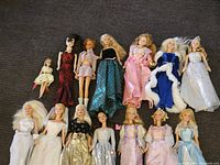 Group photo showing a total of 15 dolls mostly Barbie in various dress styles from casual to formal gowns.