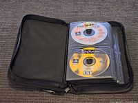 Black zippered binder with multiple PlayStation 1 discs inside protective sleeves, showing two discs: one demo and one game disc.