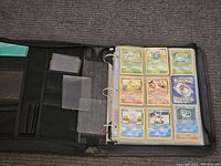 Binder open showing black zip-up 3-ring binder with interior card storage pockets and first page of card sleeves