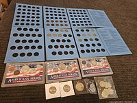 Wide view of blue coin album with vintage Indian Head pennies and Americana Series coin sets along with loose coins on a brown surface.