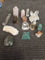 Overview of the lot showing many types of polished crystal towers, natural clusters, geode slice, and palm stone on a grey surface.