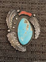 Front view of the pendant showing turquoise stone, coral inlay, silver feather designs and bead accents.