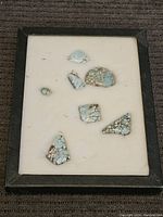 Overview of seven turquoise stones framed on cream fabric background with black border.