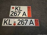 Two vintage metal license plates KL 267 A and KL : 267 A side by side on gray carpet