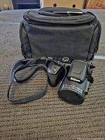 Nikon Coolpix B500 camera with attached strap in front of black carrying case, displayed on fabric surface.
