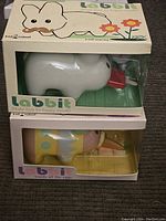 Photo showing both Kid Robot Labbit figures stacked in original boxes, white Labbit on top and colorful Labbit below.