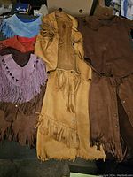 Top-down view of various southwestern style real leather clothing items stacked together showing fringe details and colors.