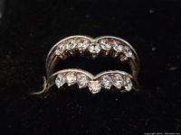 Close up of two curved sterling silver rings with small clear stones on black velvet background.