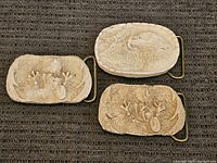 Photo of three rectangular buckles with raised animal motifs, including two with owls and one with an eagle's head on a dark textile background.