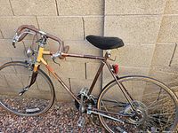 Side view of a vintage Schwinn road bicycle with drop handlebars stuck inside the frame, showing brown and yellow paint, black cushioned seat, and rear reflector.