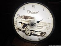 Photo showing illuminated clock face with illustrated vintage gasser drag racing car and numbers, hands visible. Clock ring is black.
