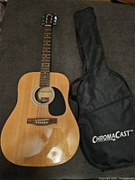 Full view of vintage Rogue acoustic guitar with natural wood finish beside ChromaCast branded black gig bag on gray surface.