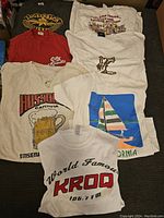 Overview of seven vintage graphic T-shirts in various colors and designs stacked on a couch.