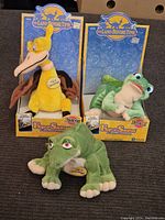 Three Land Before Time plush toys, two displayed in original packaging with a third green plush laid in front.