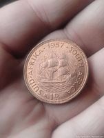 Obverse side of 1957 South Africa large penny coin showing sailing ship and inscriptions.