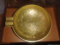 Top-down view of round brass ashtray showing floral etching and rests for cigarettes or cigars.