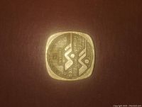 Obverse side of square metal Olympic coin token with shooting event text and pictogram.