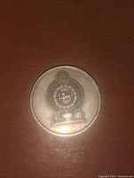 Obverse side of the one rupee coin showing a circular emblem with a lion figure and decorative elements.