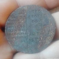 Front side of the iron token showing text 'THE BROKEN COIN', '20 REELS', and '15 WKS' with significant rust and wear.