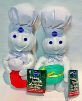 Two Pillsbury Doughboy beanie plush toys, one holding green gift box, other holding red stocking