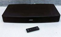Front view of black Bose Solo TV Sound System soundbar with original remote control placed in front of it.
