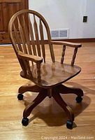 Solid oak swivel office chair showing complete front and side view with curved back slats, armrests, and caster wheels.