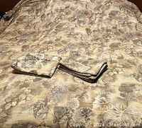 King size comforter laid flat with two matching pillow shams folded on top showing floral and grapevine pattern in beige, tan, mauve, and gold tones.