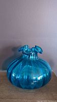 Front view of the translucent blue turquoise glass onion shaped vase showing the optic ribbed texture and the flared, ruffled mouth opening.