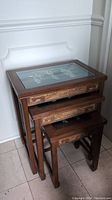 Set of three vintage Asian carved wood nesting tables with glass tops showing the diorama carvings beneath.