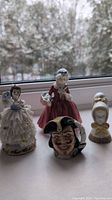 Four porcelain figurines shown together: lace princess, Lavinia, Captain Henry Morgan mug, Young Amish Bust