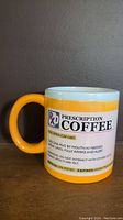 Side shot of full mug showing orange handle and prescription coffee label graphic on white ceramic surface