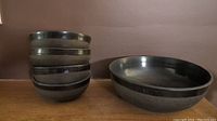 Five dark glazed pottery bowls shown: one large bowl on the right and four smaller bowls stacked on the left