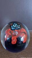 Front view of clear spherical glass paperweight showing the red flower and blue polka dot butterfly inside.