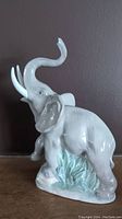 Full side view of the white elephant figurine with trunk raised and leafy base.
