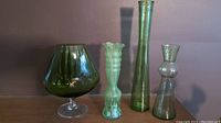 Photo showing all four vintage green glass vases with varied shapes and sizes against a plain background
