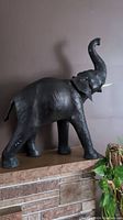 Full side view showing the large elephant wrapped in black leather with raised trunk and tusks.