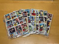 Photo of 6 uncut sheets of 1984 Topps baseball cards displayed on a wooden surface. Sheets are in plastic protective sleeves. Players visible include Nolan Ryan and Cal Ripken.