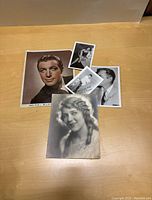 Five vintage fan photos displayed on a wooden table, including a large colorized Robert Taylor photo and smaller black and white photos of other Hollywood stars