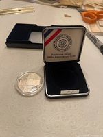 1992 White House silver dollar proof coin displayed next to velvet-lined presentation box with presidential seal and anniversary text.