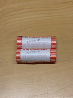 Two unopened rolls of $10 quarters labeled 2009 DC-D on a wooden surface