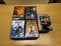 Photo showing DVDs 'Notes on a Scandal,' 'Prisoners,' 'Coming to America,' 'Black Snake Moan,' and 'The Bourne Supremacy' arranged in stacks on a wooden table.